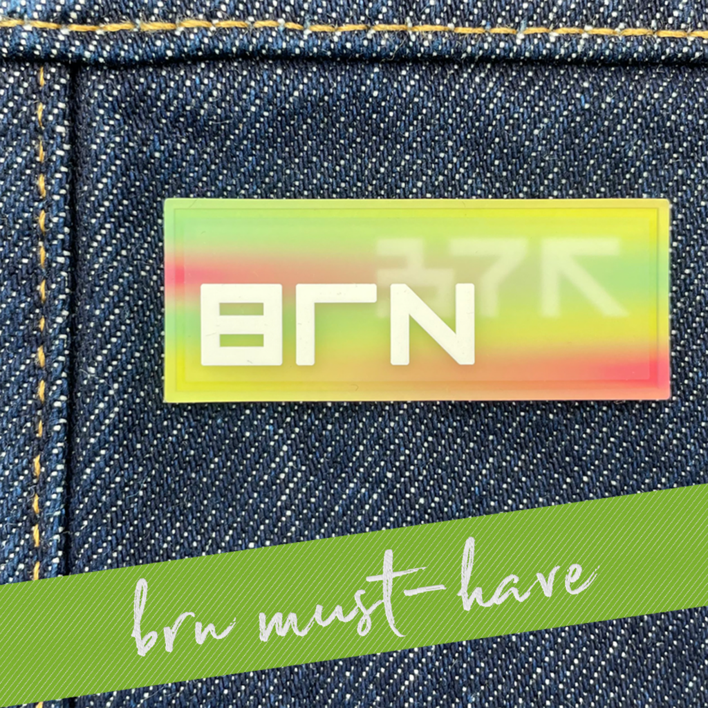 Silicone label with a gradient in rainbow colors and lettering BRN. The label in applied to a denim fabric. 