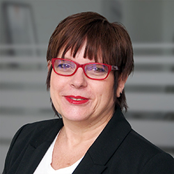 Lächelnde Frau mit dunklen Harren und einer roten Brille. Heidi Volkmann - Head of HR